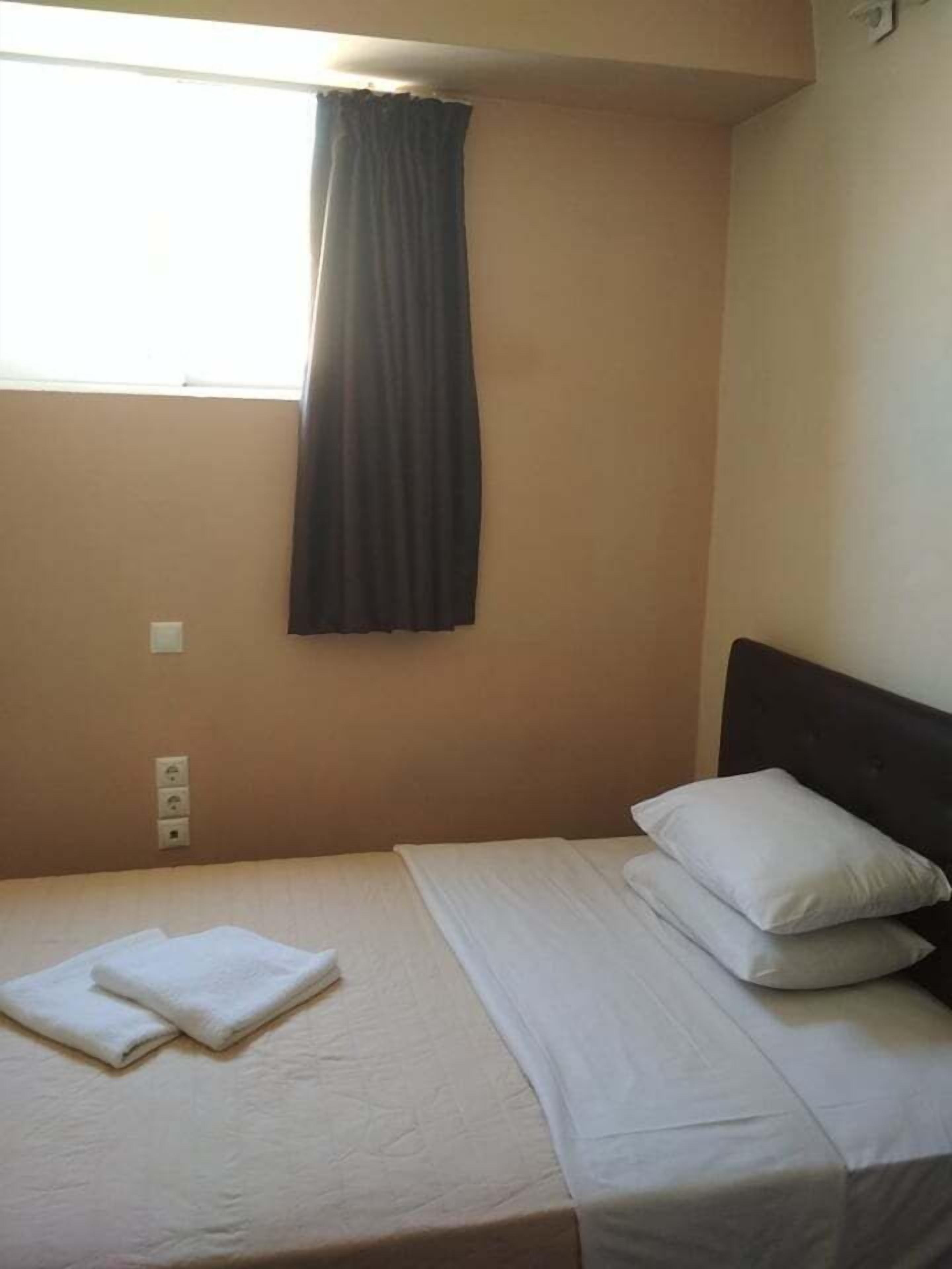 A single bed with white bedding and pillows, a window with a dark curtain, and a wall socket.