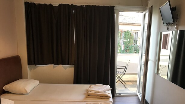 A hotel room with a bed, a chair, a TV, and a view of the outside. - Pella Inn Hostel (Athens)