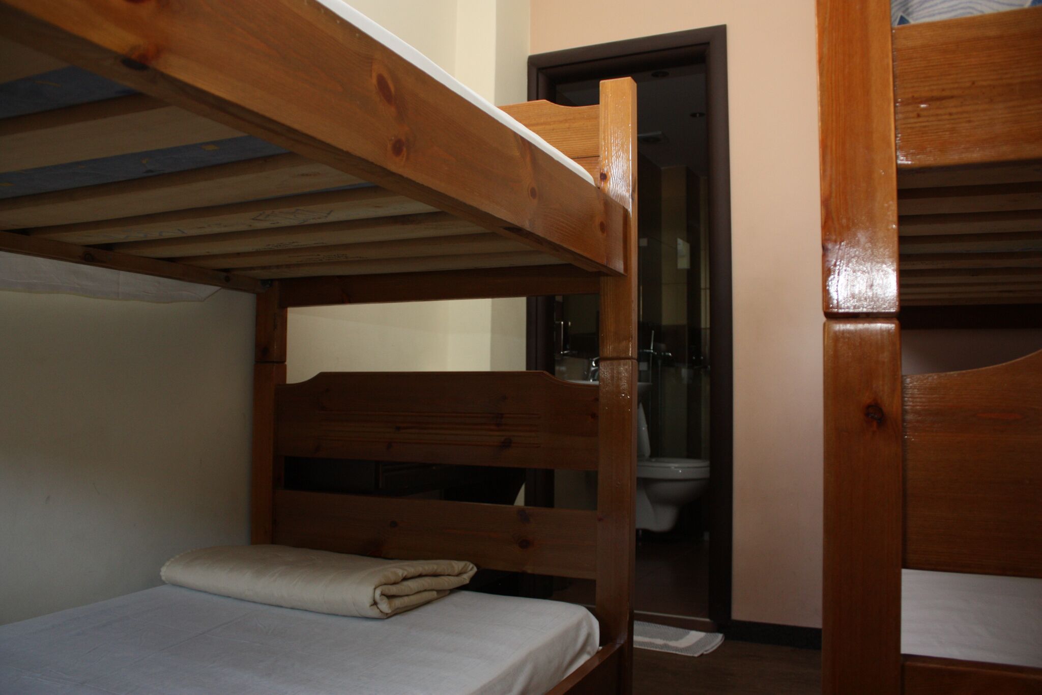A bunk bed room with a wooden headboard, a small bedside table, and a door leading to a bathroom.