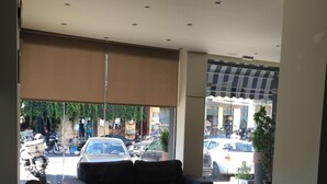 A modern lobby with a sofa and coffee table, large windows with a view of the street, and a ceiling with recessed lighting. - Pella Inn Hostel (Athens)