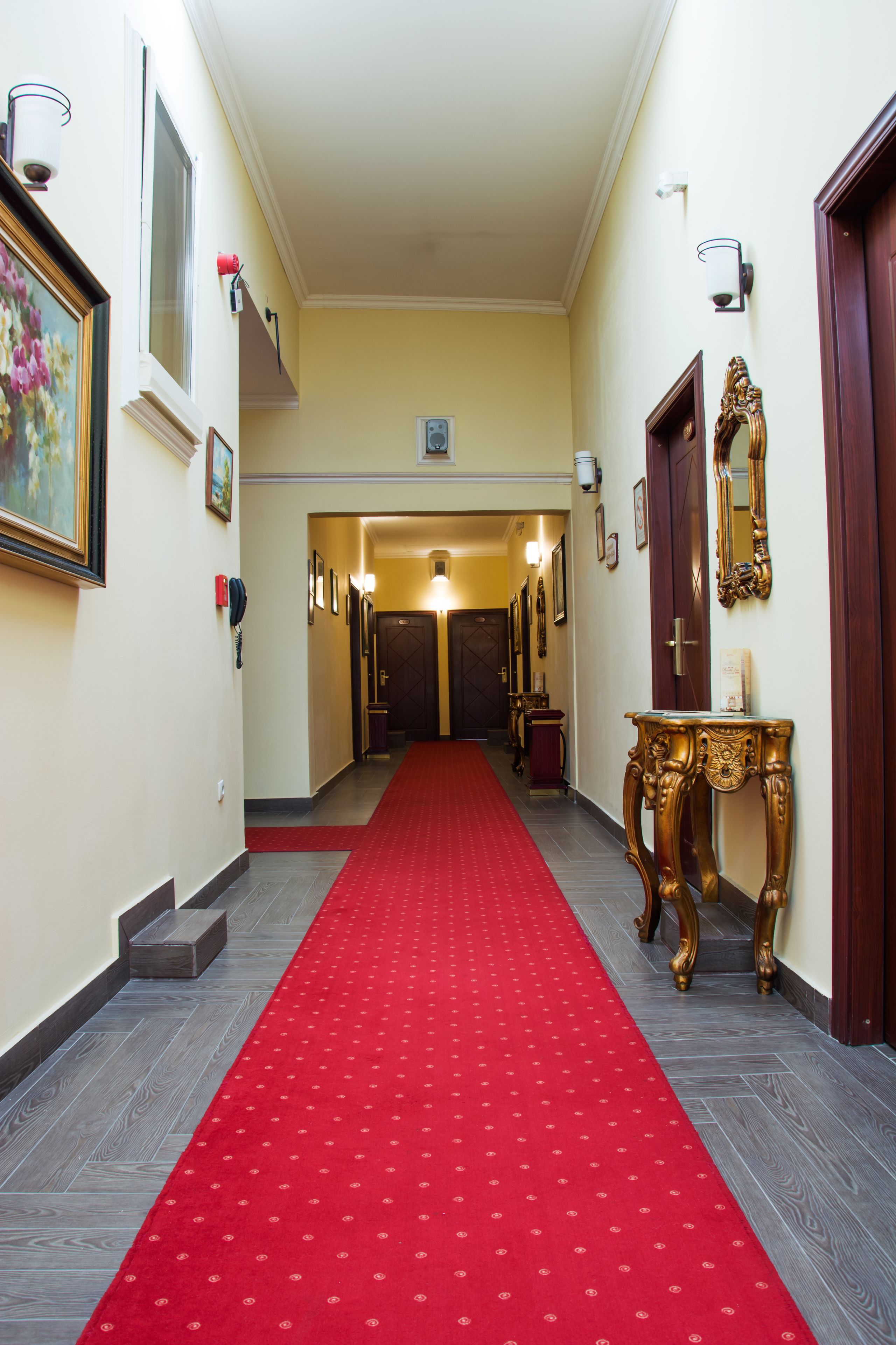 A hotel hallway with a red carpet, wooden floors, and a large mirror on the right.