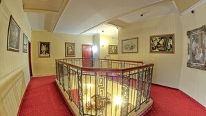 A grand hallway with a red carpet, a glass railing, and framed artwork on the walls. - Planeta Inn Hotel (Novi Sad)