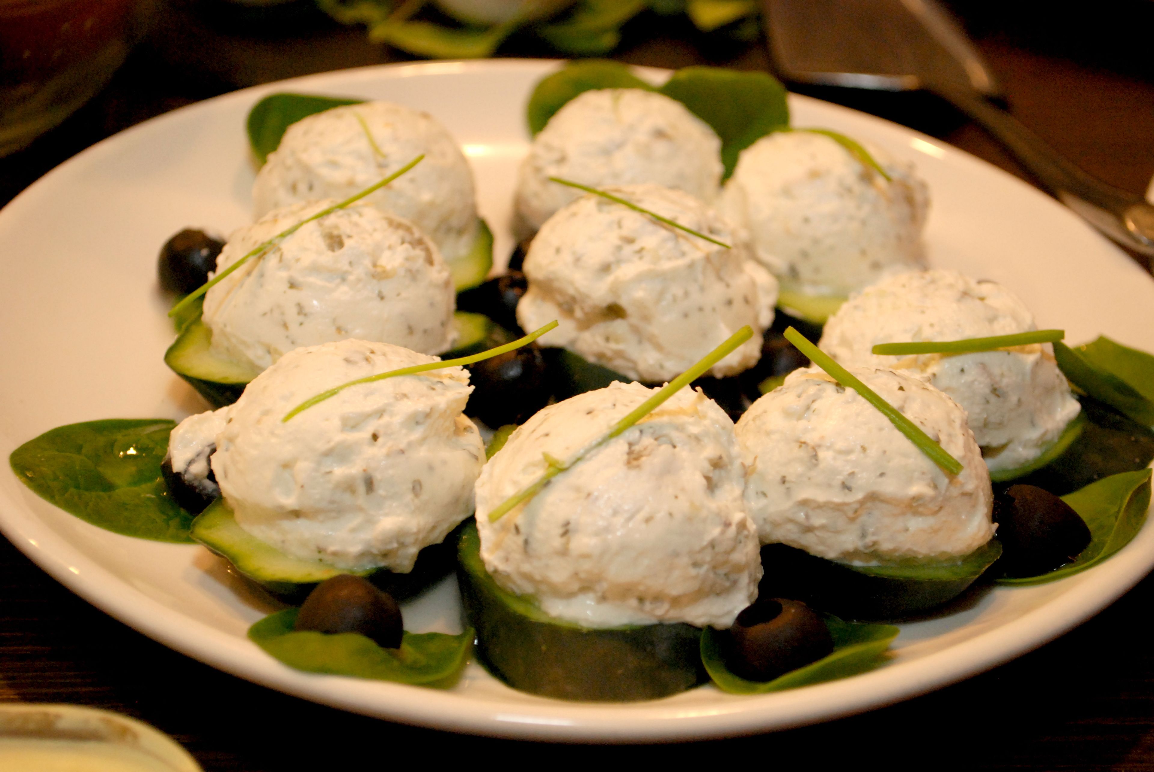 Un piatto di cibo con fette di avocado ricoperte da una crema bianca, guarnito con erbe aromatiche.