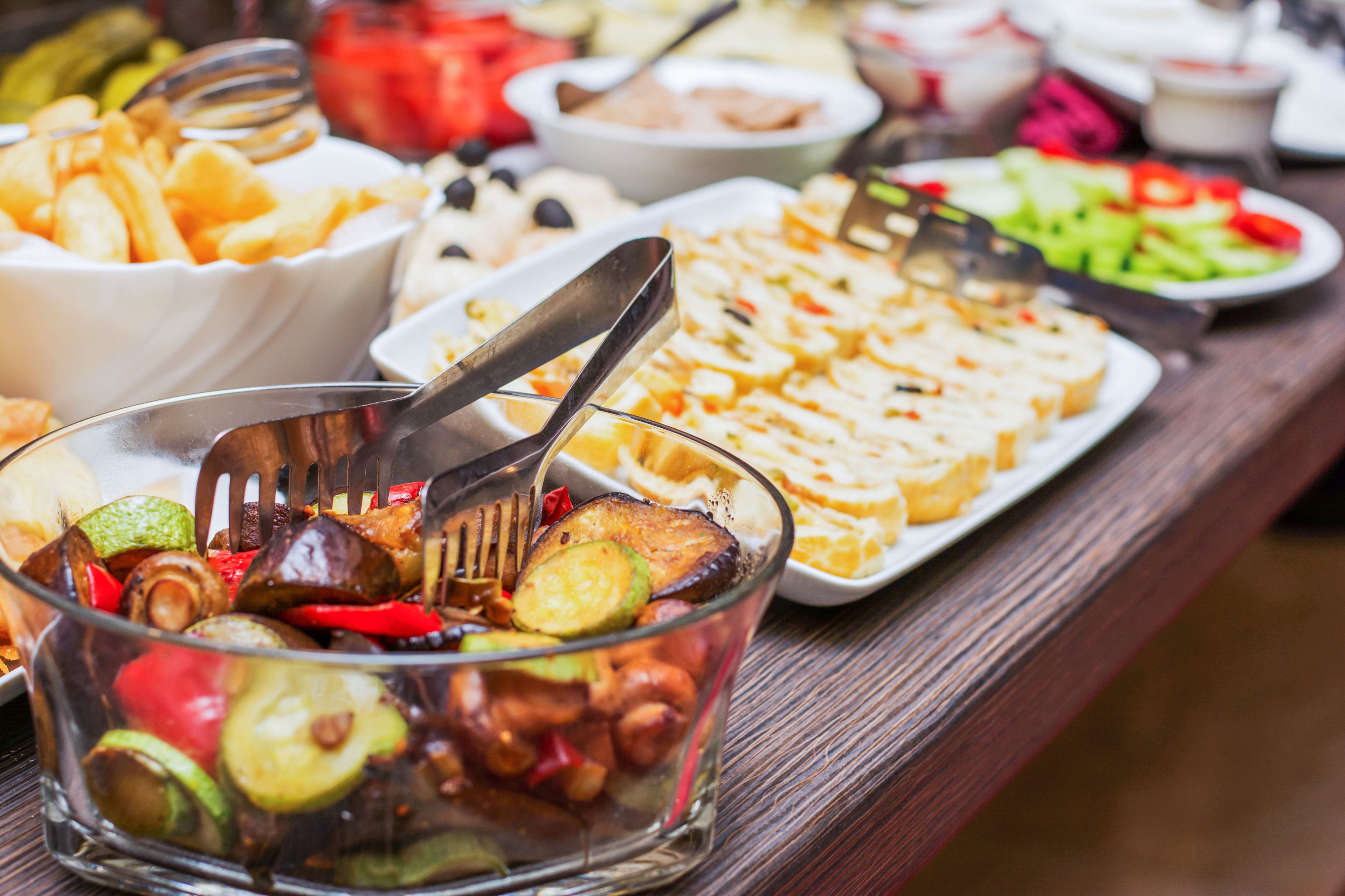 Una mesa de buffet con diversos platos, incluyendo un bol de verduras mezcladas, un plato de pan en rebanadas y otros alimentos.