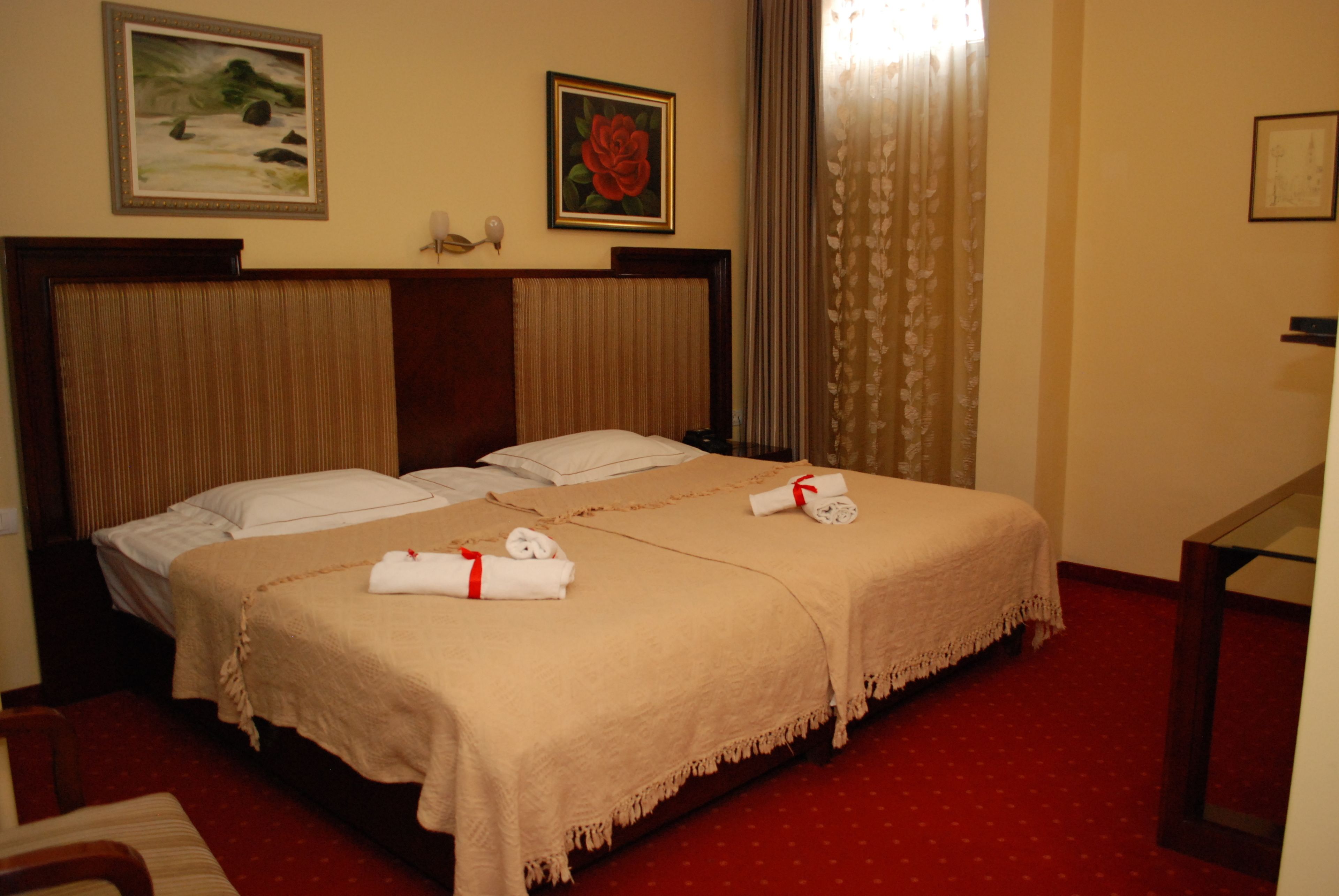 A hotel room with two beds, a wooden headboard, a red carpet, and artwork on the walls.