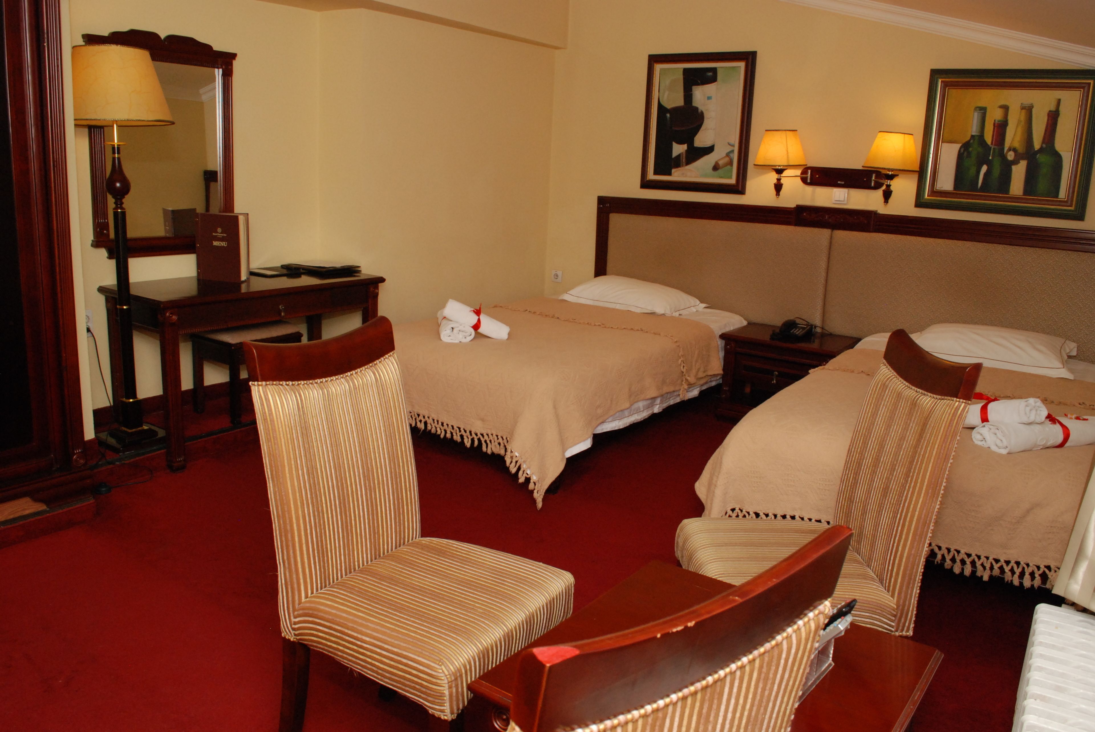 Habitación de hotel con dos camas, un escritorio, una silla, una lámpara y obras de arte en las paredes.