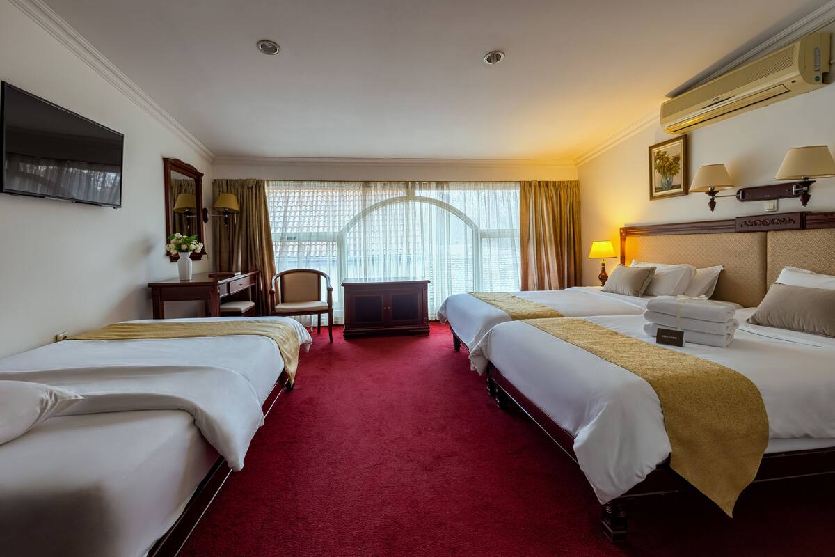 Habitación de hotel con dos camas, un escritorio, una silla, un televisor y un ventanal con cortinas.