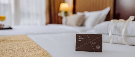 A neatly made bed with white linens, a brown placard with the hotel name, and a lamp in the background.