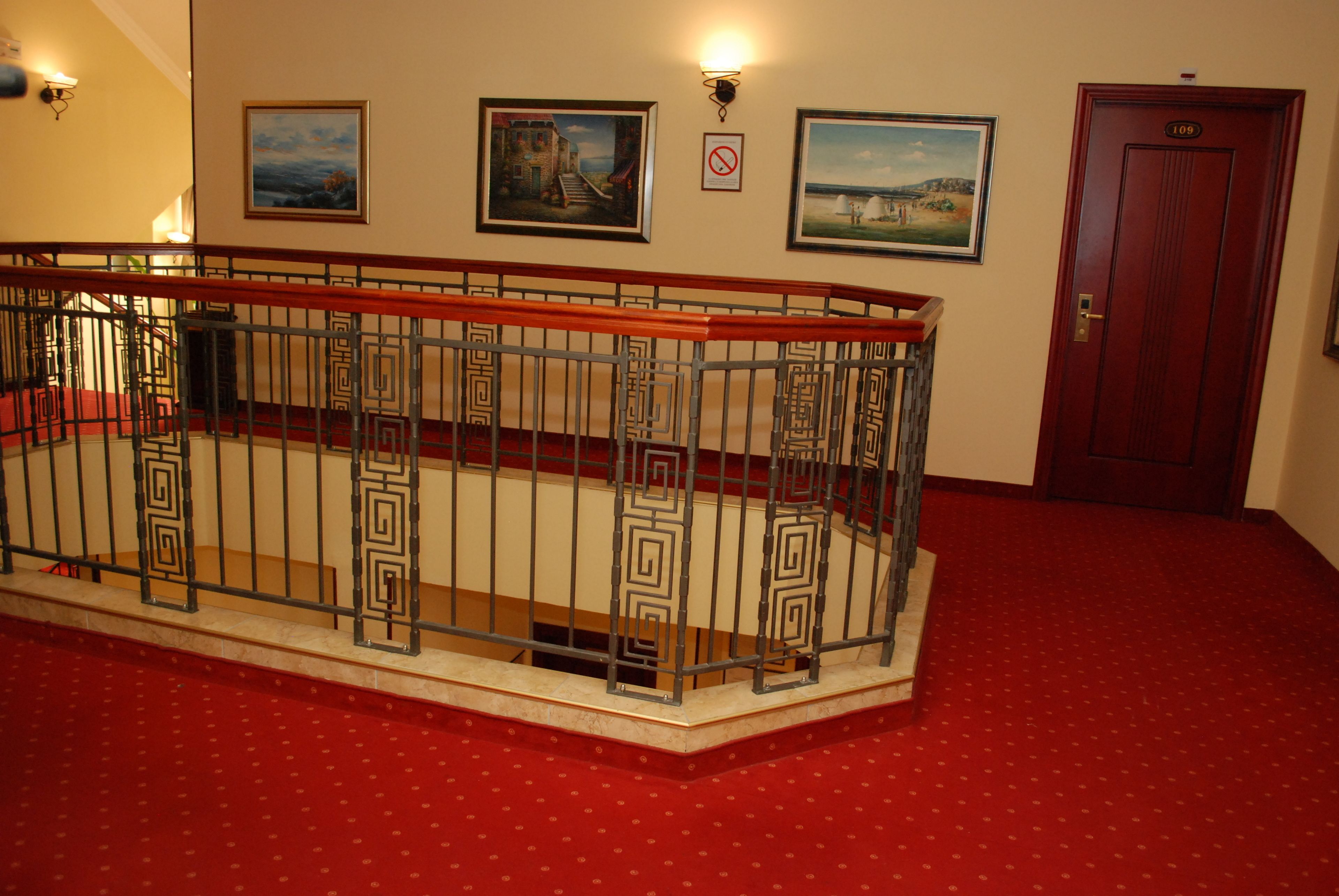 A staircase with a metal railing, a red carpeted floor, and three framed pictures on the wall.