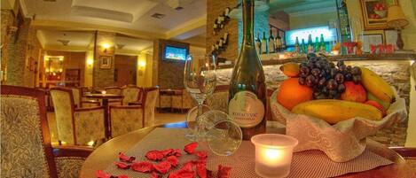 A dining table with a bottle of KOVACEVIC Chardonnay, a candle, and a bowl of fruit.