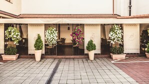 A building entrance with a tiled patio, potted plants, and hanging flower arrangements.