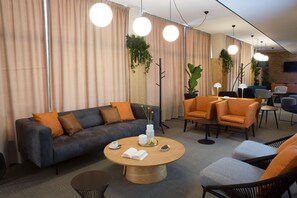 Uma área de estar moderna com um sofá cinzento, poltronas laranjas, uma mesa de centro de madeira e uma mesa de jantar com cadeiras.