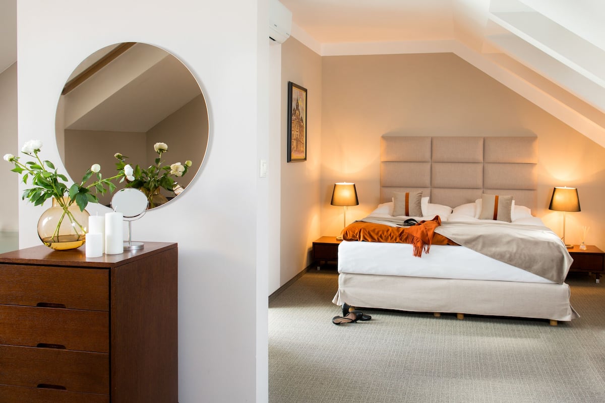 Une chambre à coucher avec un lit, des lampes de chevet, une commode, un miroir et un vase avec des fleurs.