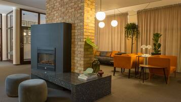 A modern living room with a fireplace, a sofa, a dining table with chairs, and a large plant.