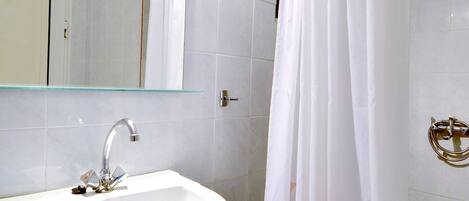 Un baño con lavamanos blanco, espejo y cortina de ducha.