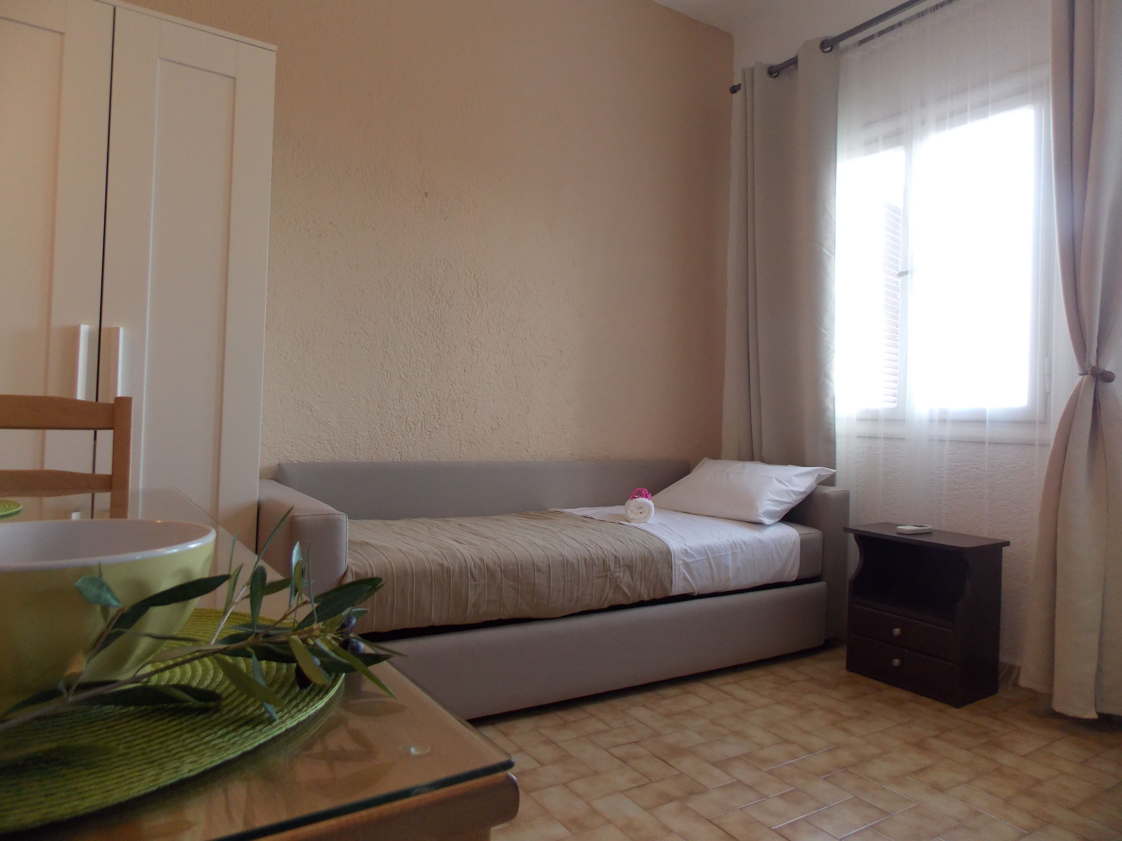 A bedroom with a bed, a bedside table, a chair, and a window with curtains.