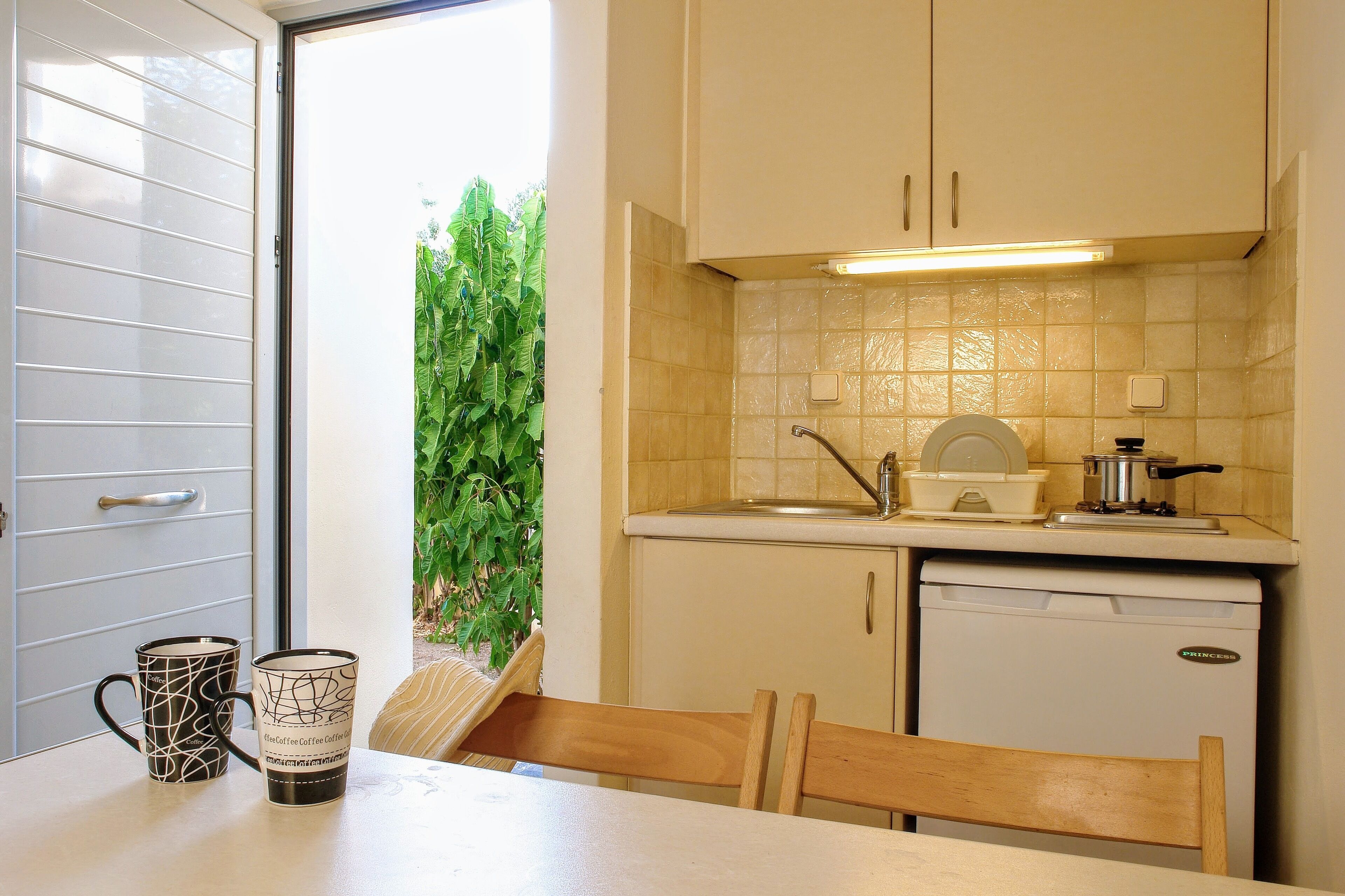 A compact kitchen with a sink, a small refrigerator, and a window with a view of greenery.