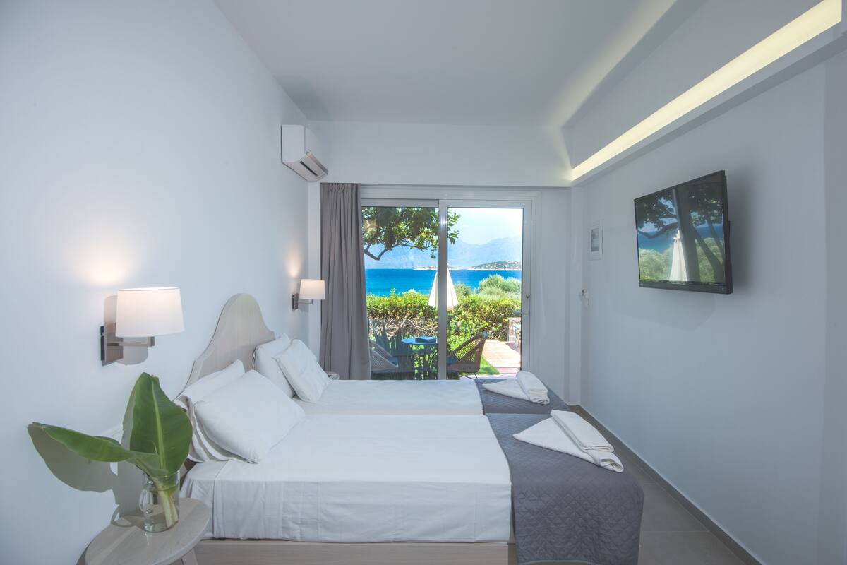 Ein Hotelzimmer mit Bett, Nachttisch mit Lampe, Pflanze und Meerblick.