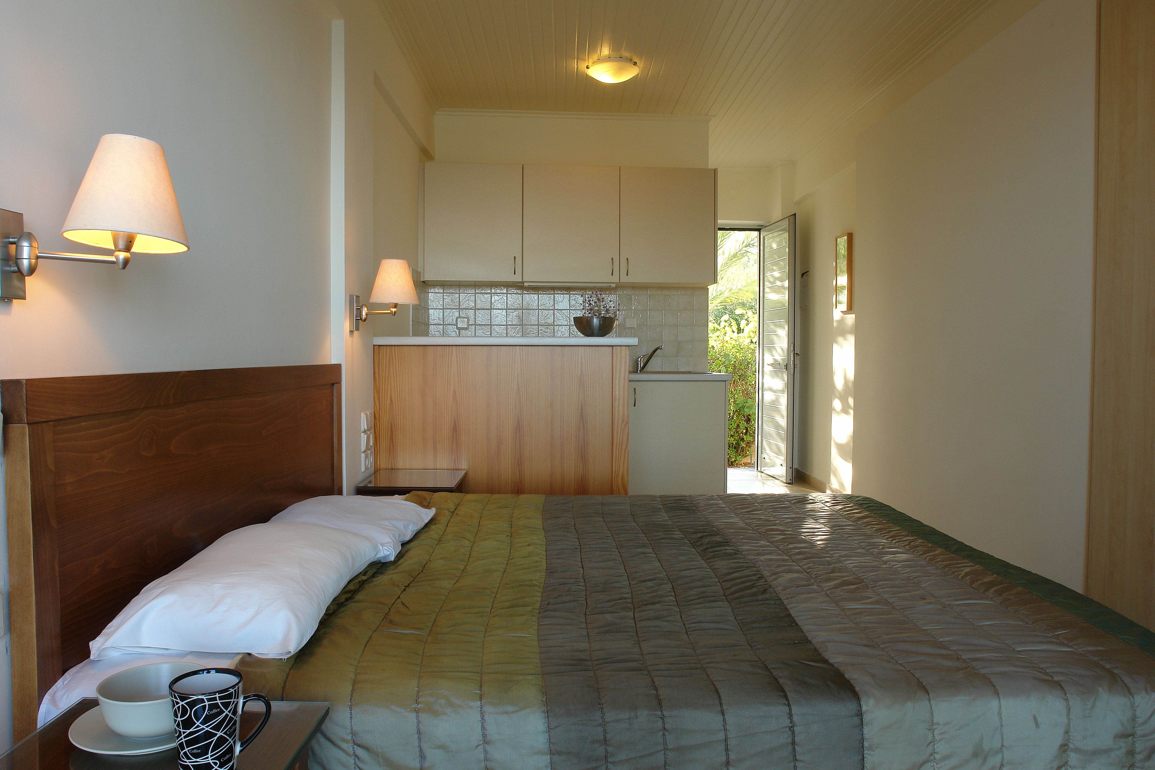 A bedroom with a bed, bedside table, and a view of the kitchen.