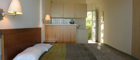 A bedroom with a bed, bedside table, and a view of the kitchen.