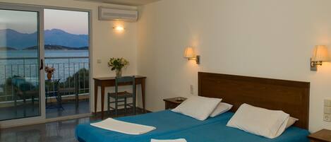 A hotel room with a large bed, a desk, and a view of the sea.