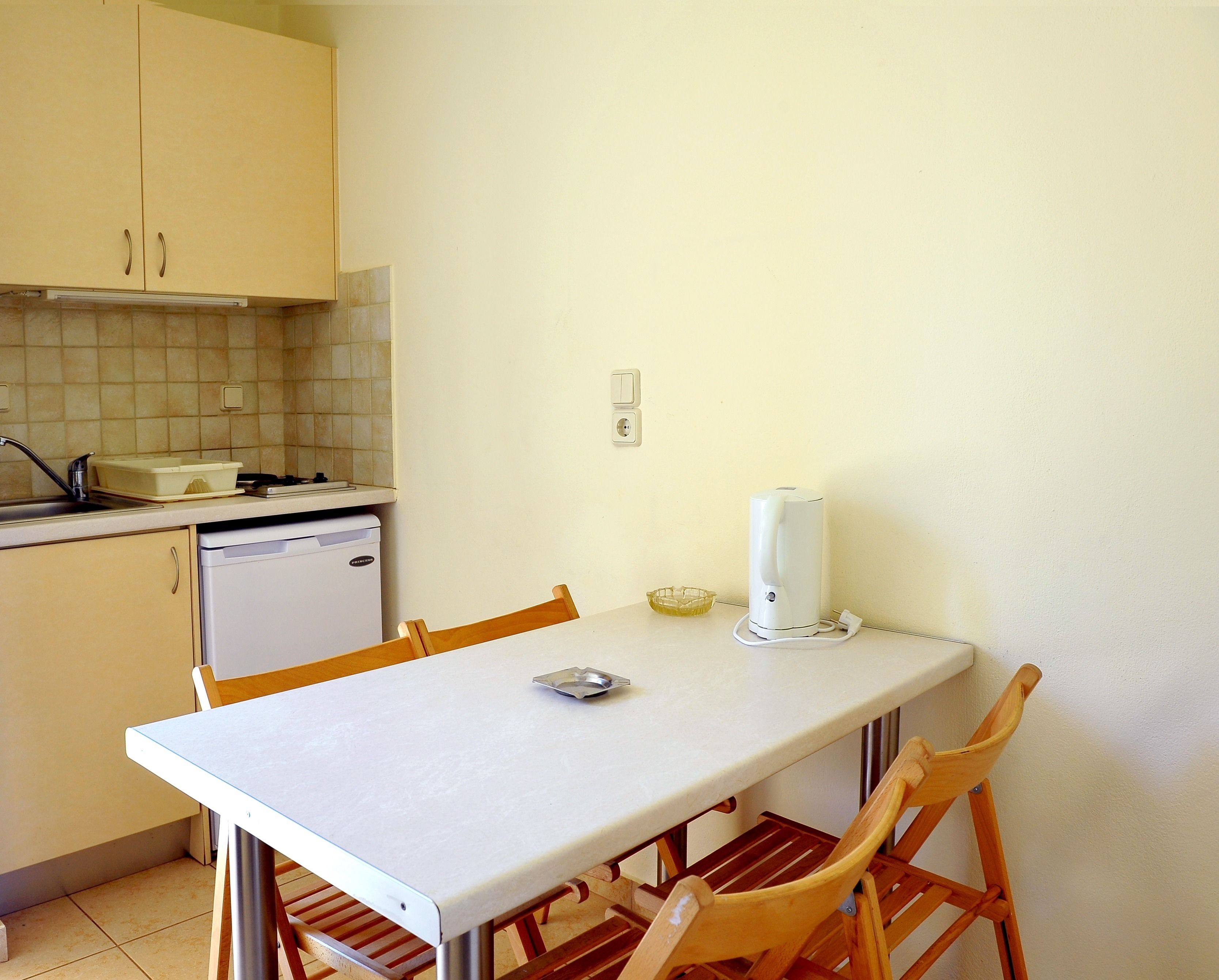 A small kitchen with a table and chairs, a refrigerator, a microwave, and a kettle.