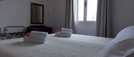 Una habitación de hotel con cama, dos toallas, cómoda, espejo y ventana con cortinas.