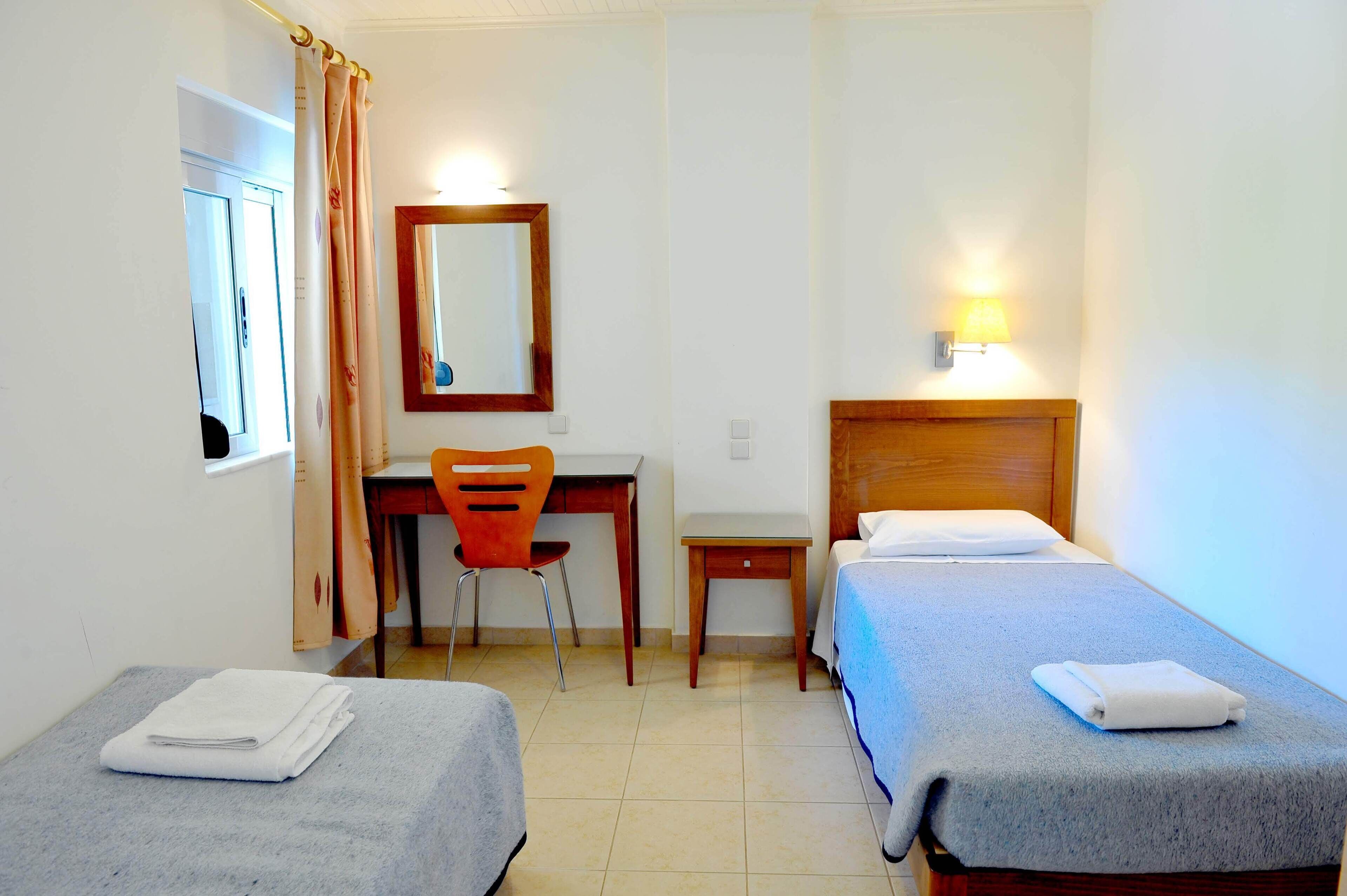 Een hotelkamer met twee eenpersoonsbedden, een bureau met stoel, een spiegel en een klein tafeltje.