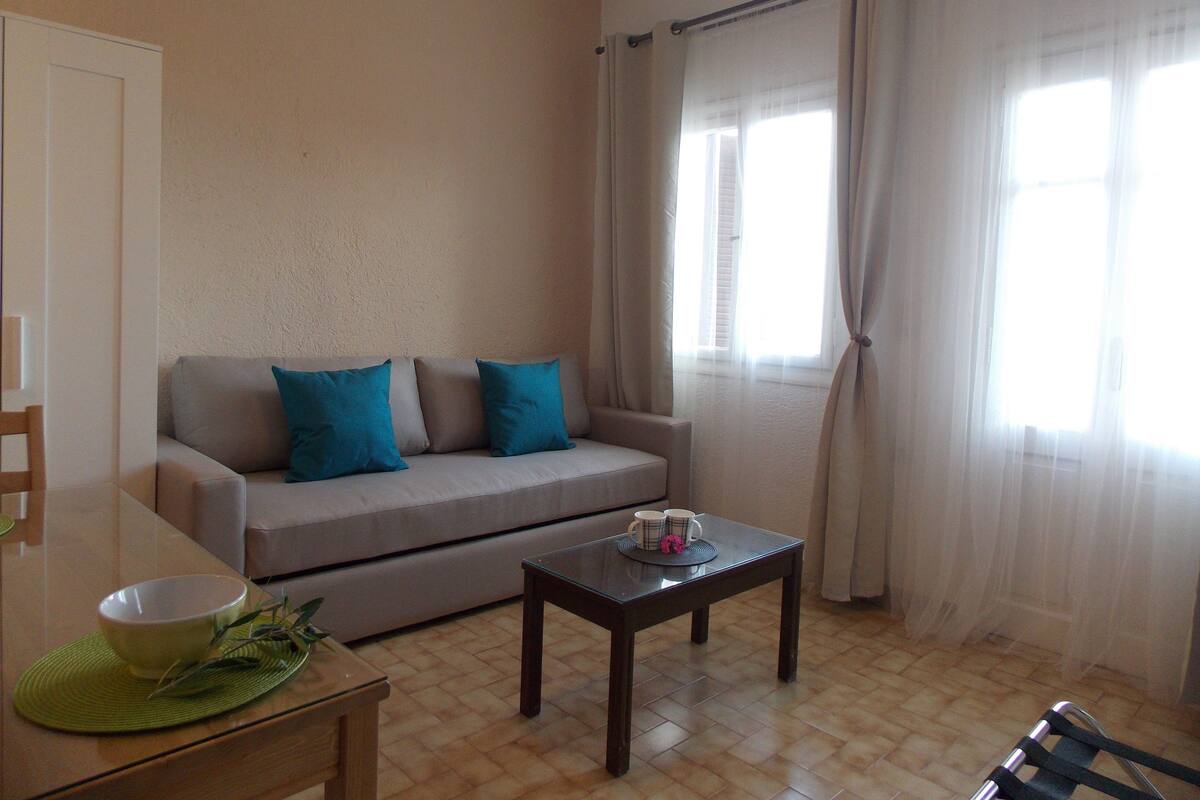 Ein Wohnzimmer mit einer Couch, einem Couchtisch und einem Esstisch mit Schüssel und Pflanze.