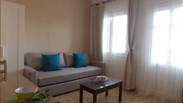 A living room with a sofa, a coffee table, and a dining table with a bowl and a plant.