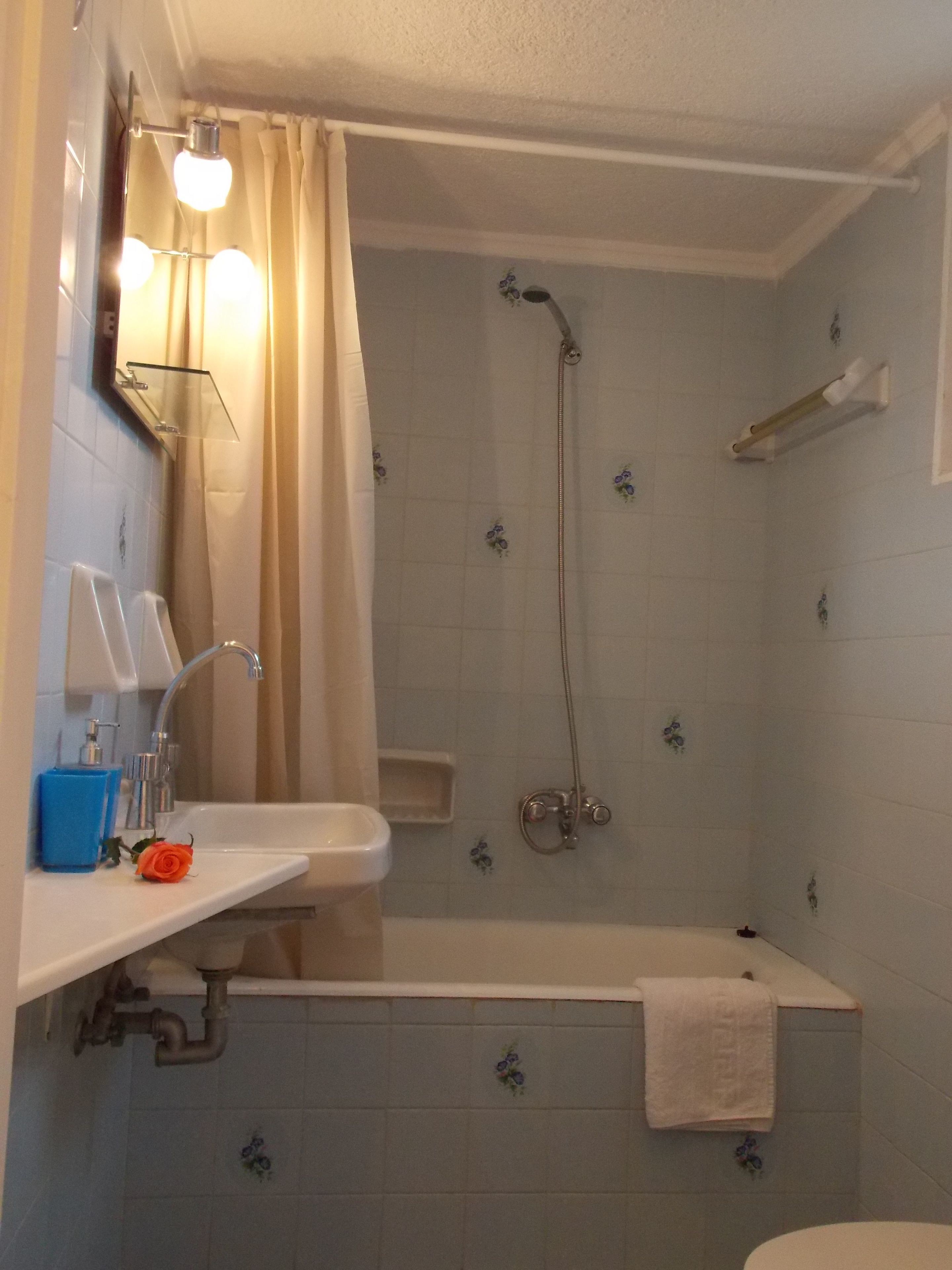 Un baño con bañera, ducha, lavamanos con espejo y una toalla colgada en la pared.