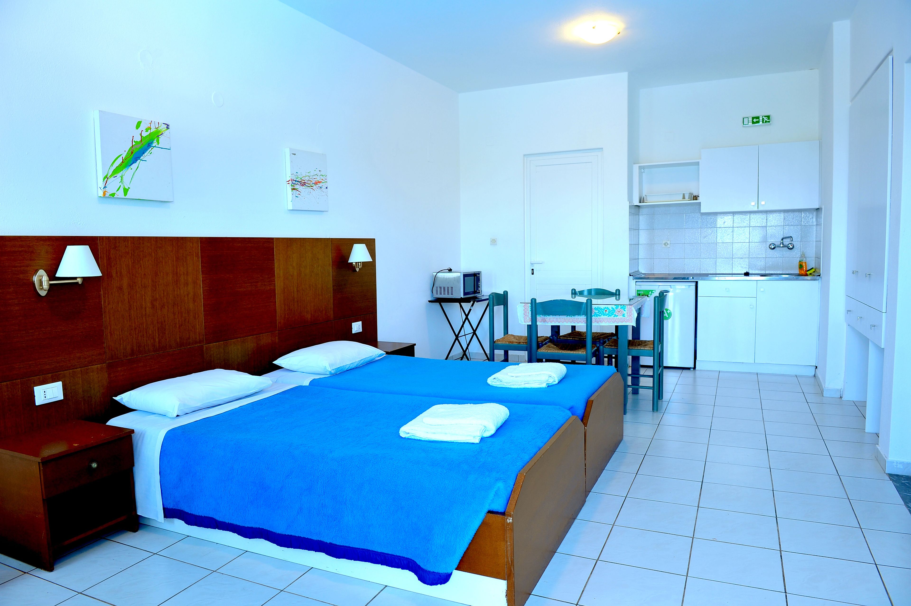 A hotel room with two beds, a small kitchenette, and a dining area.