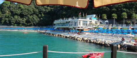 A coastal hotel with a pool area, a lifeguard tower, and a red boat docked near the shore.