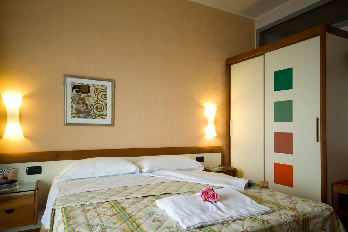 A hotel room with a bed, a nightstand, a wall-mounted lamp, and a door with a geometric design.