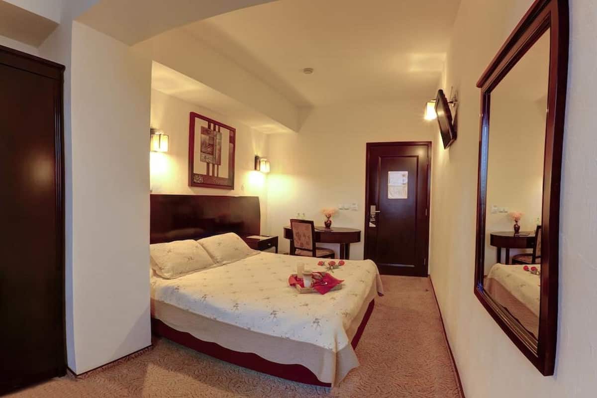 Une chambre d’hôtel comprenant un lit, des tables de chevet, un bureau, une chaise, un miroir et une porte.