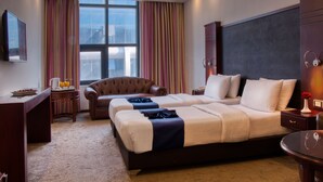 A hotel room with a large bed, a desk, a chair, and a view of the city through the window. - Torino Amman Hotel (Amman)