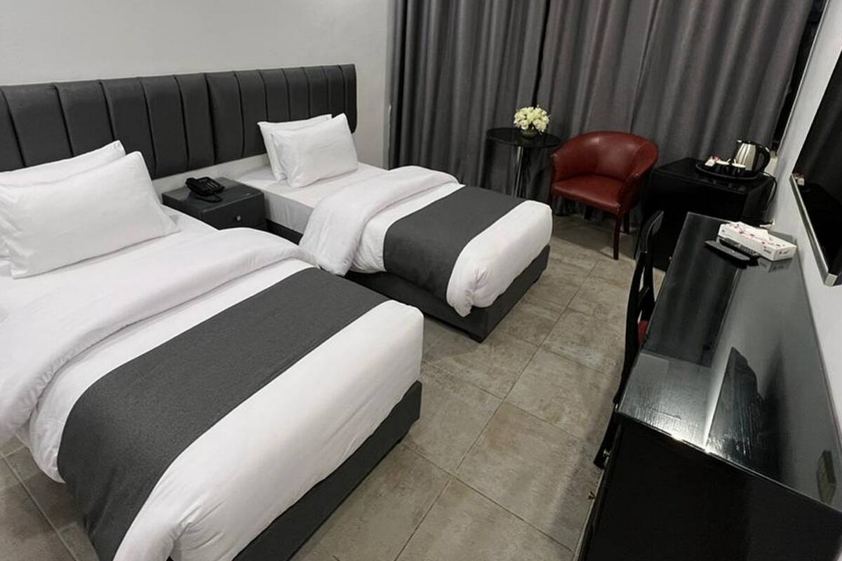 A hotel room with two beds, a desk, a chair, a TV, and a window with curtains.