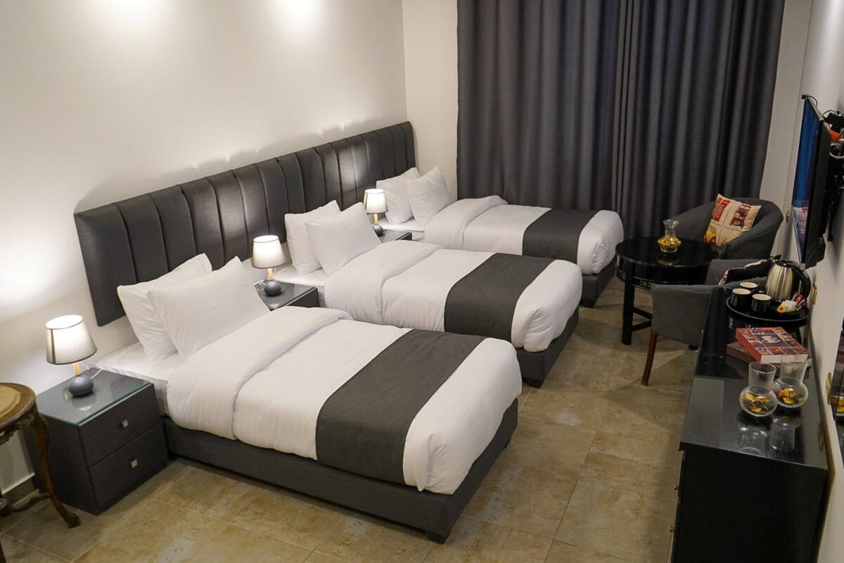 A hotel room with two beds, a desk, a chair, a nightstand, and a lamp.