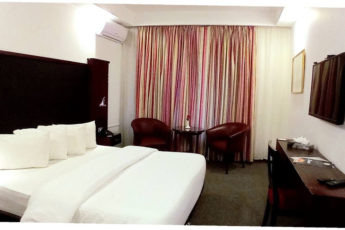 A hotel room with a large bed, two chairs, a small table, a desk, a TV, and a curtain with vertical stripes.