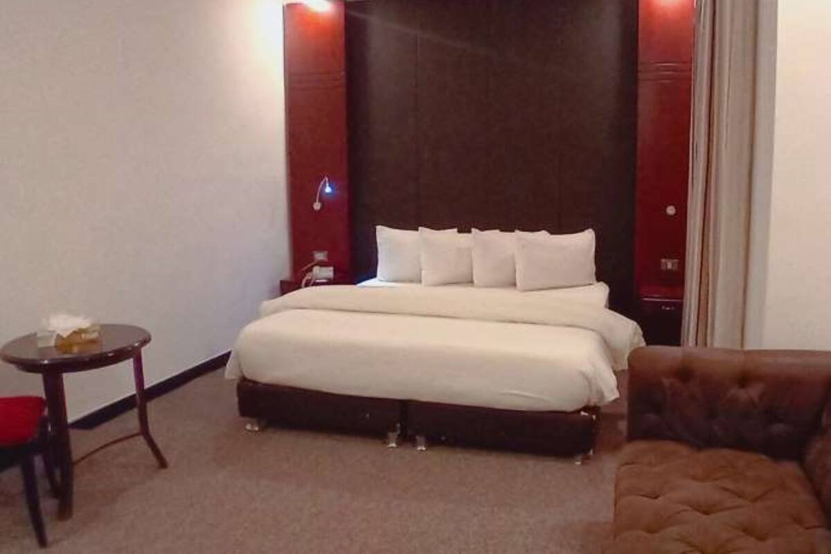 A hotel room with a large bed, a small table with a tissue box, and a brown armchair.