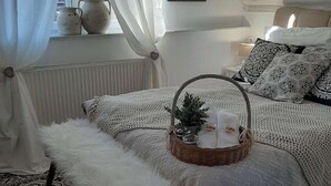 Un dormitorio acogedor con cama, un banco blanco y mullido, una cesta de mimbre con una planta y una alfombra estampada.
