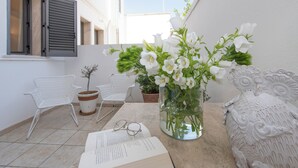 A small balcony with a white chair, a potted plant, a vase with flowers, and an open book. - Hotel Albània (Otranto)