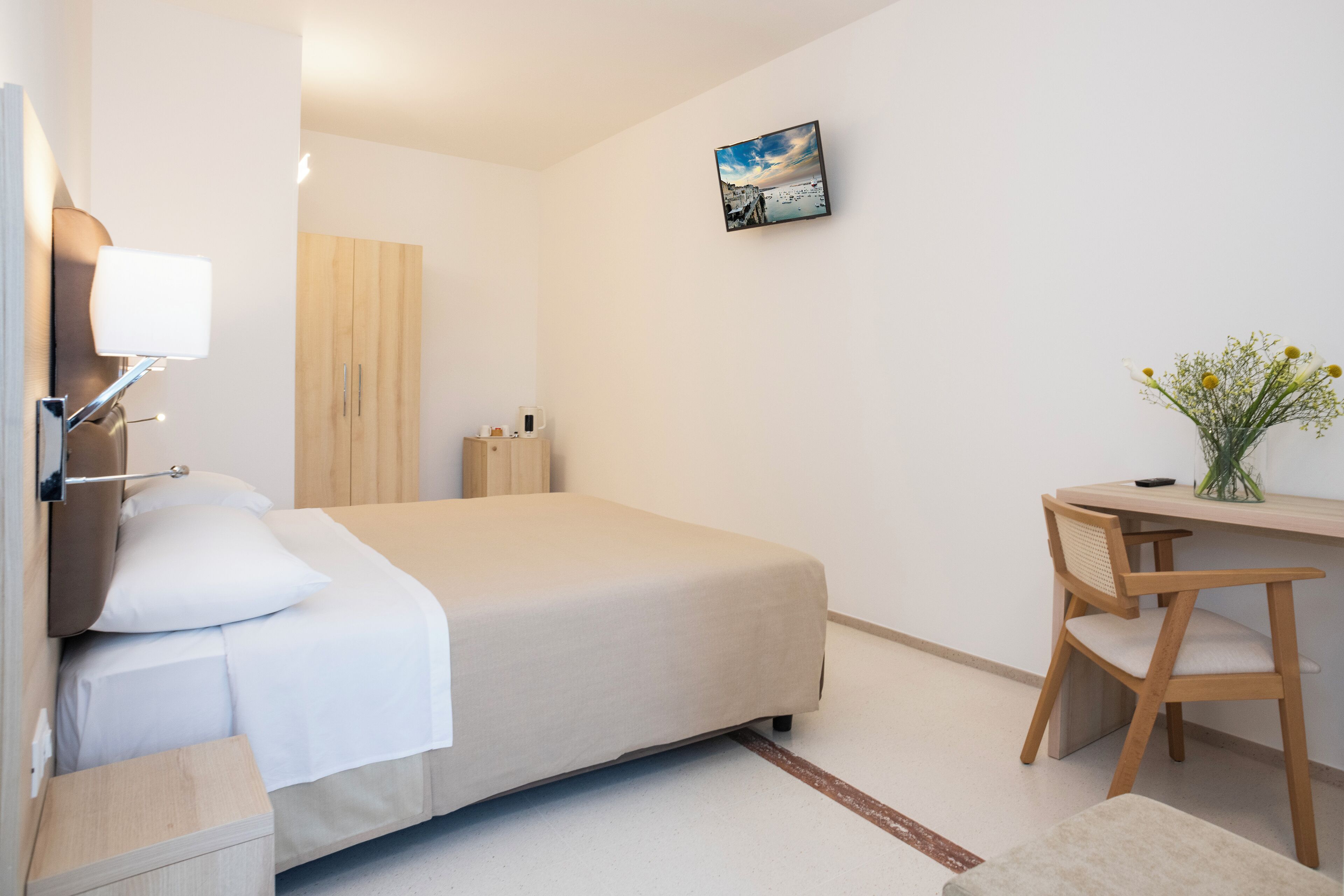Camera da letto minimalista con un letto, comodino, lampada e una scrivania con sedia.