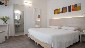 Un dormitorio moderno con cama de madera, una mesita de noche con un teléfono, un espejo y un baño visible a través de una puerta abierta.
