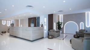 A modern reception area with a marble reception desk, several sofas, and a large potted plant. - Hotel Albània (Otranto)