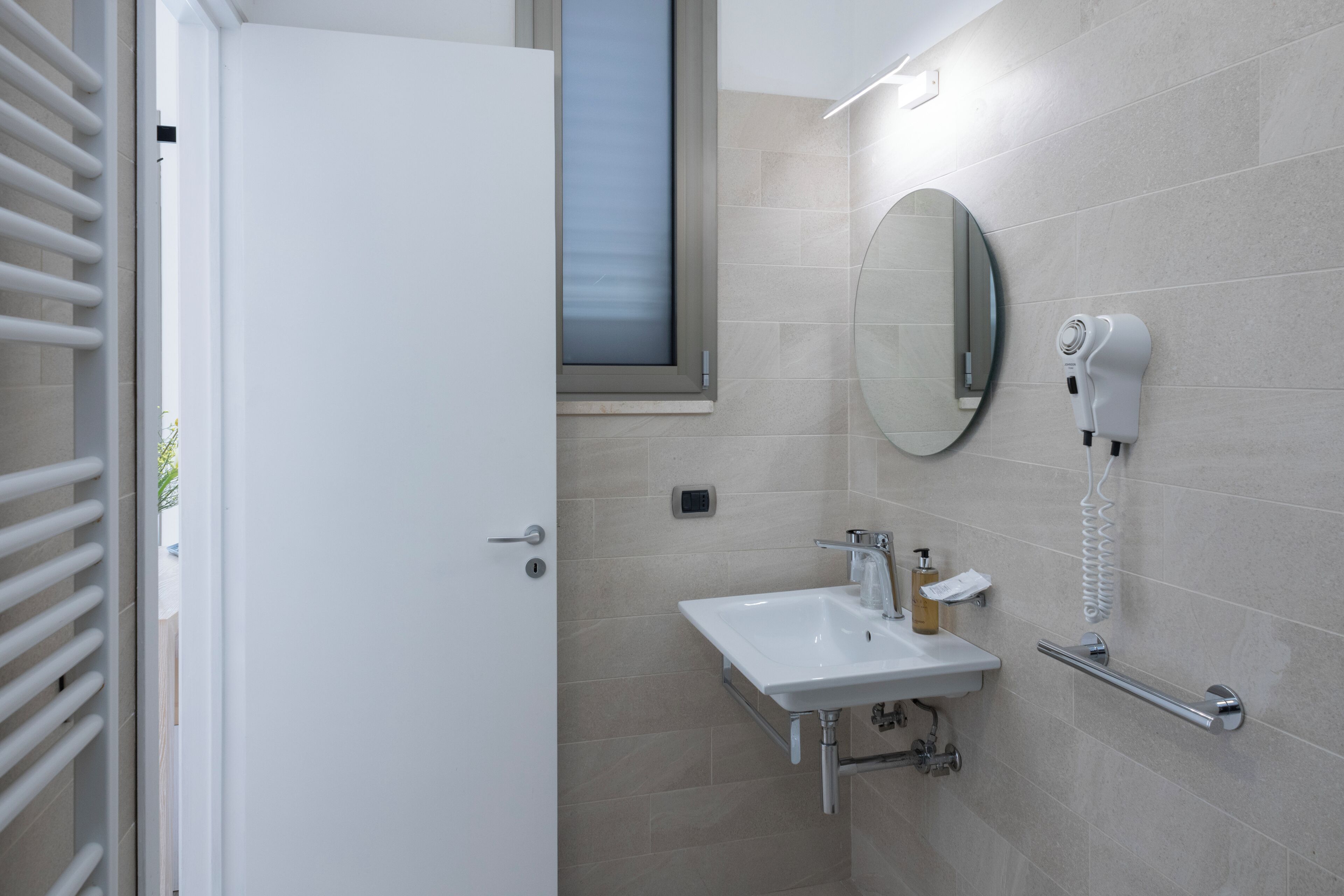 A modern bathroom with a white sink, a mirror, and a hairdryer mounted on the wall.
