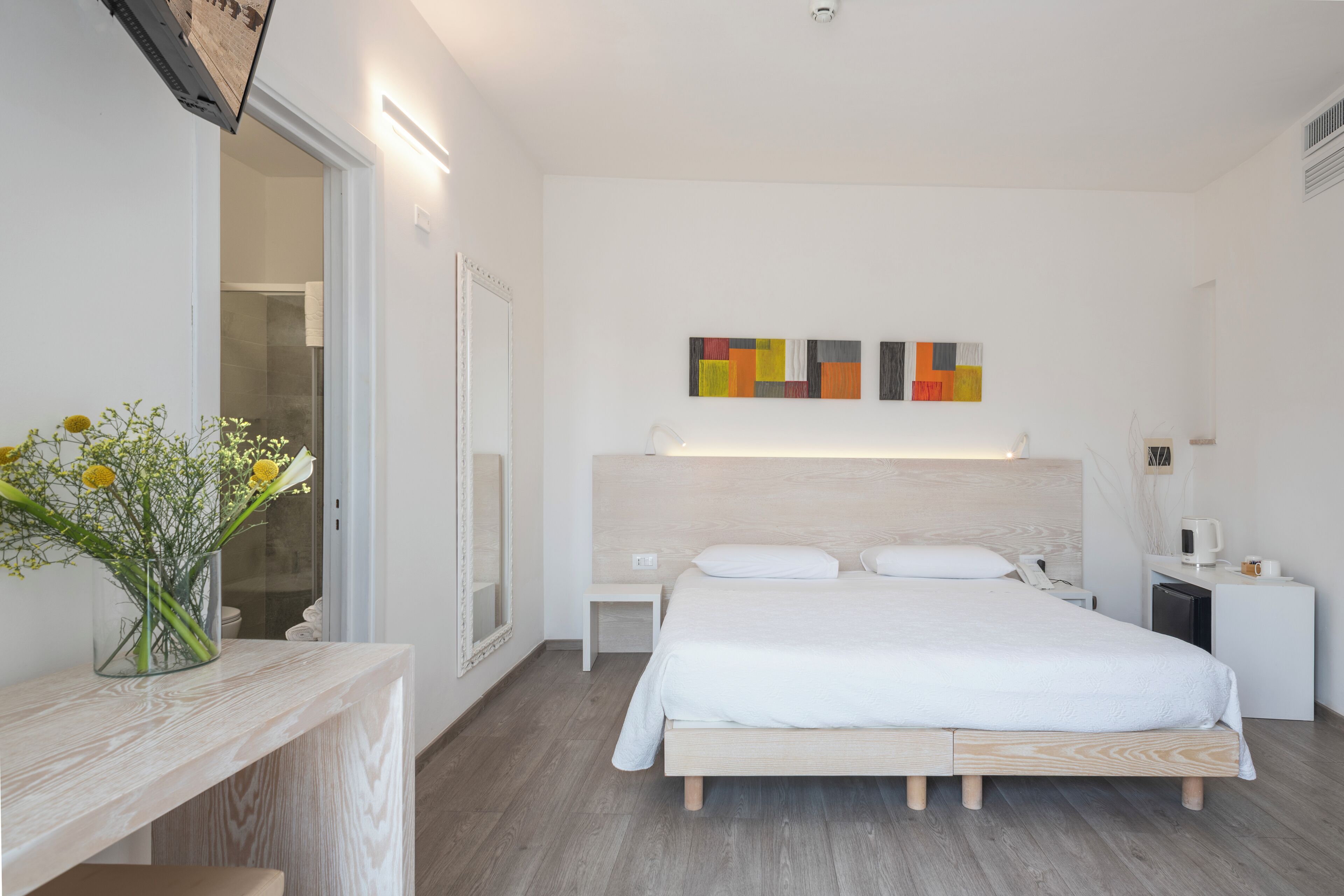 Quarto de hotel moderno com uma cama grande, mesas de cabeceira, uma pequena escrivaninha e uma obra de arte pendurada na parede.