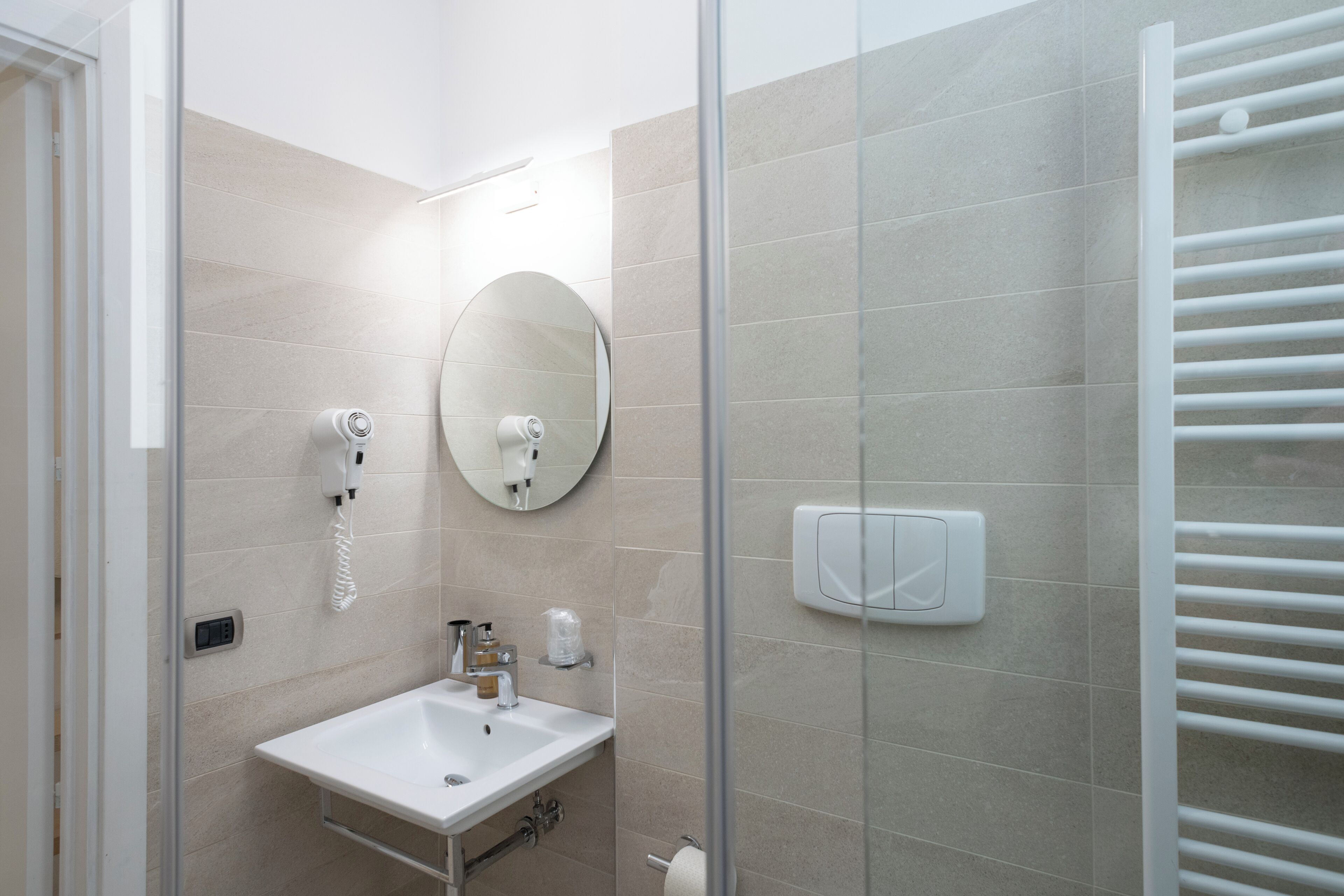 A modern bathroom with a glass partition, a sink, a mirror, a towel rack, and a soap dispenser.
