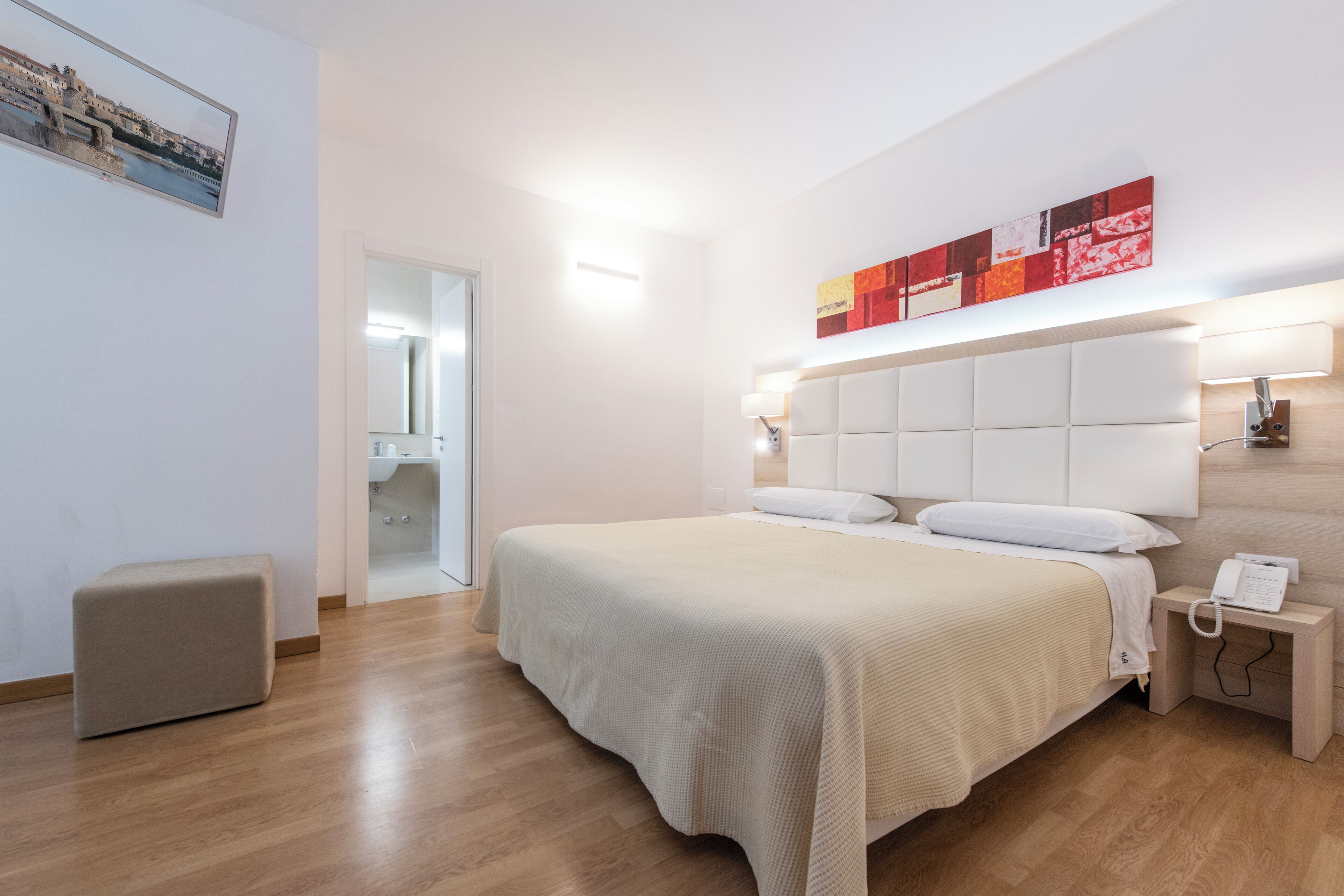 Quarto de hotel moderno com uma cama grande, mesa de cabeceira e um quadro na parede.