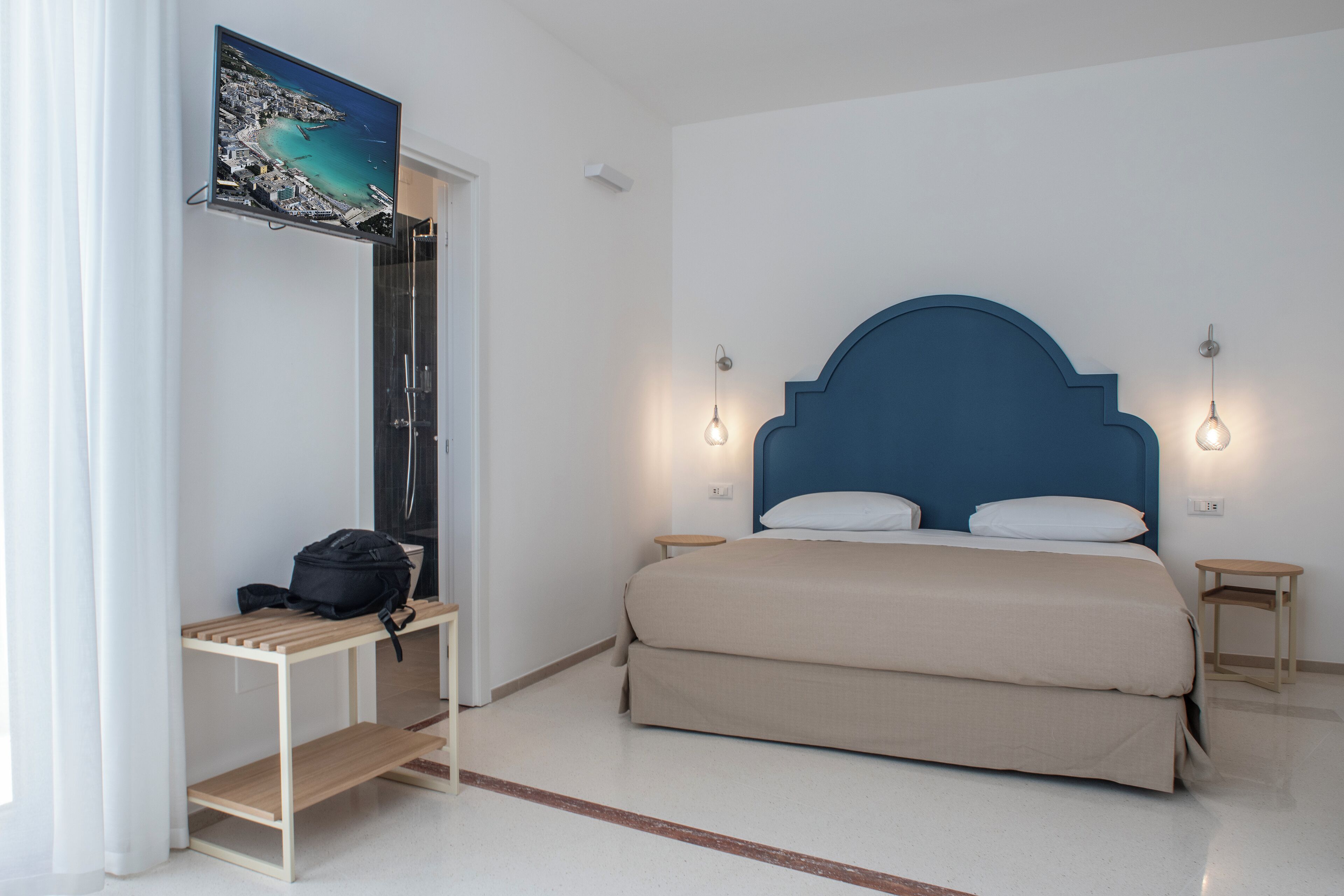 A bedroom with a bed, a TV mounted on the wall, bedside tables, and a bench.